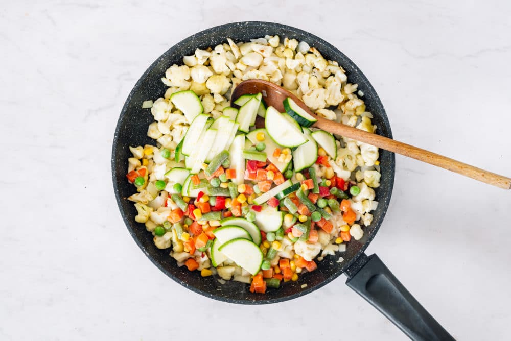 Zucchini and frozen veggies atop cauliflower rice in a skillet.