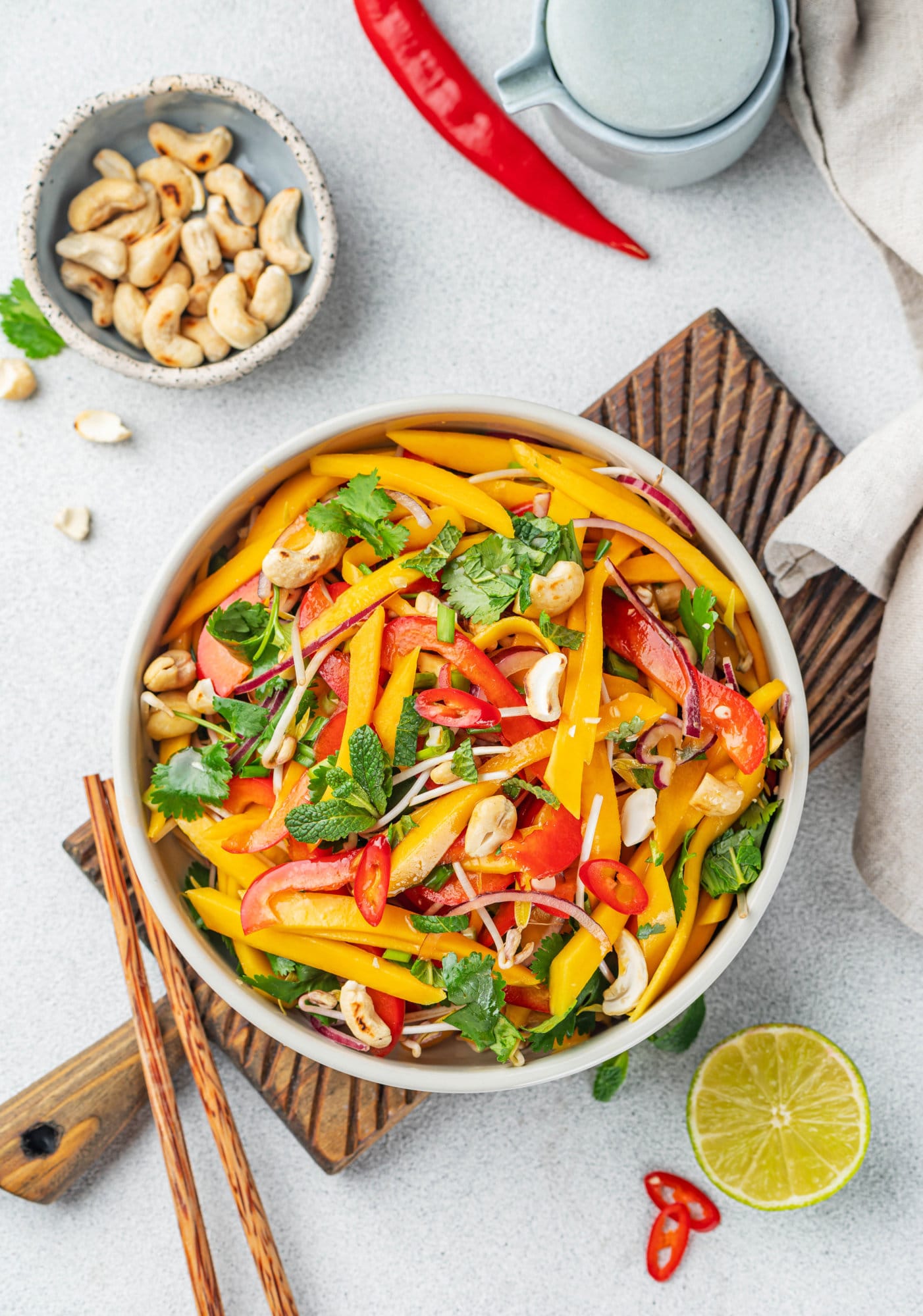 Thai salad in a white bowl on a wooden board with chopsticks on the side.