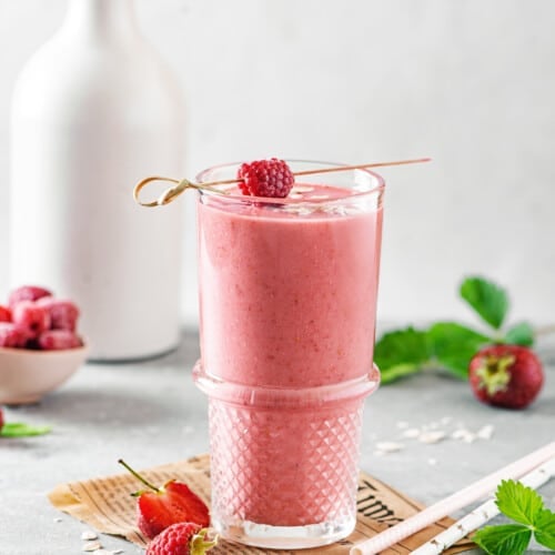 a glass filled with berry smoothie on brown paper with raspberries and strawberries in the background.