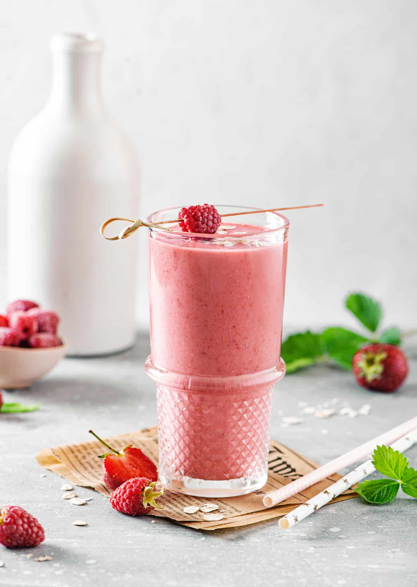 a glass filled with berry smoothie on brown paper with raspberries and strawberries in the background.