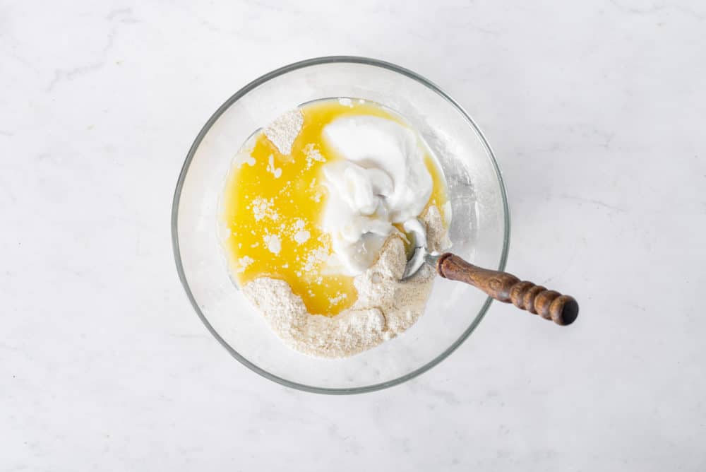 Peach cobbler dough mixing in a glass bowl with a spoon.