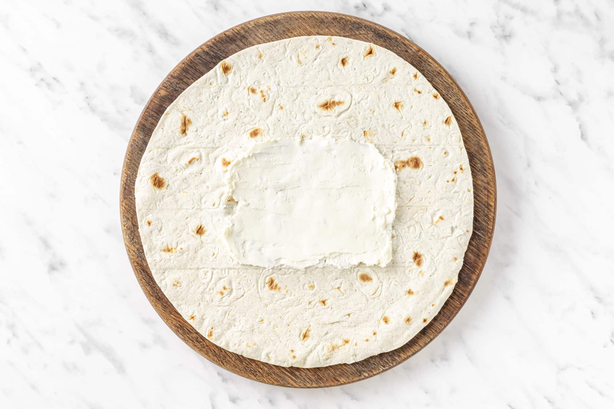 a tortilla with cream cheese in the center spread out.