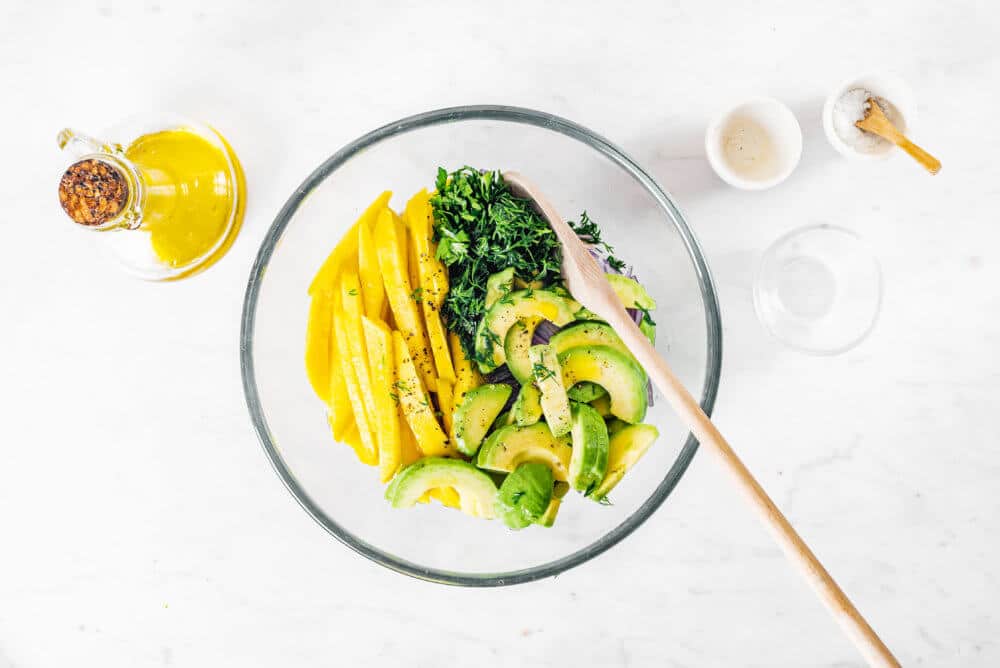 avocado-chicken-salad-being-mixed-in-a-glass-bowl-with-a-wooden-spoon-with-olive-oil-on-the-side