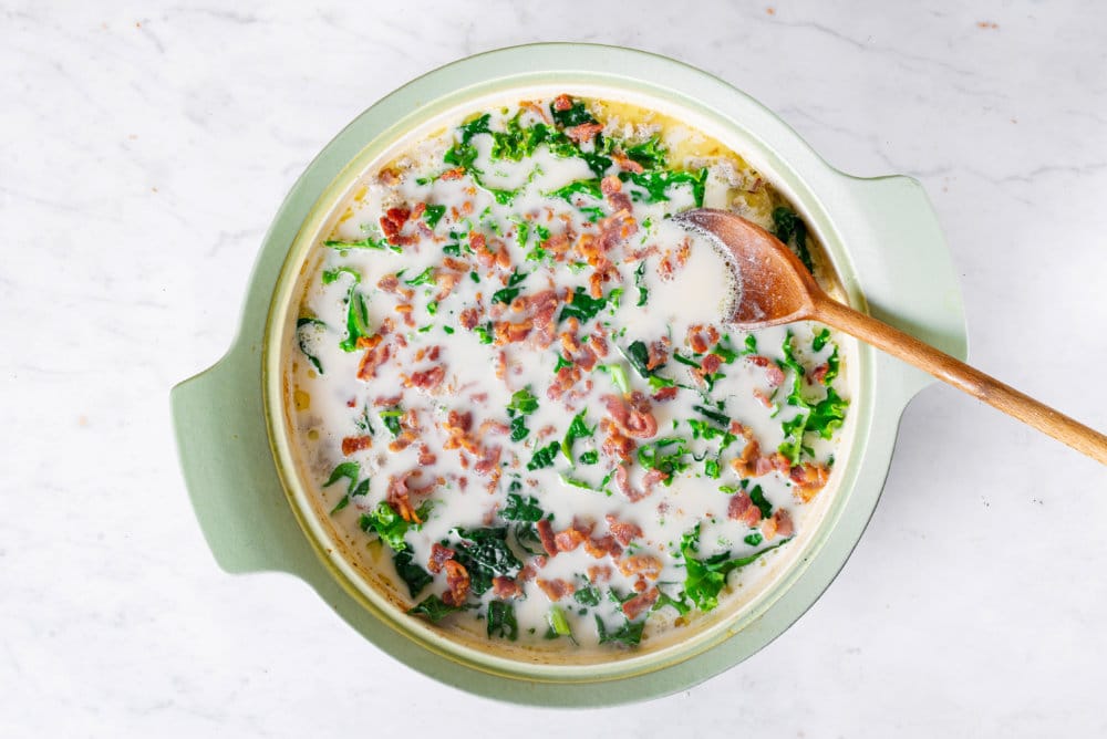 Zuppa toscana soup in a large green pot freshly cooked with a spoon.