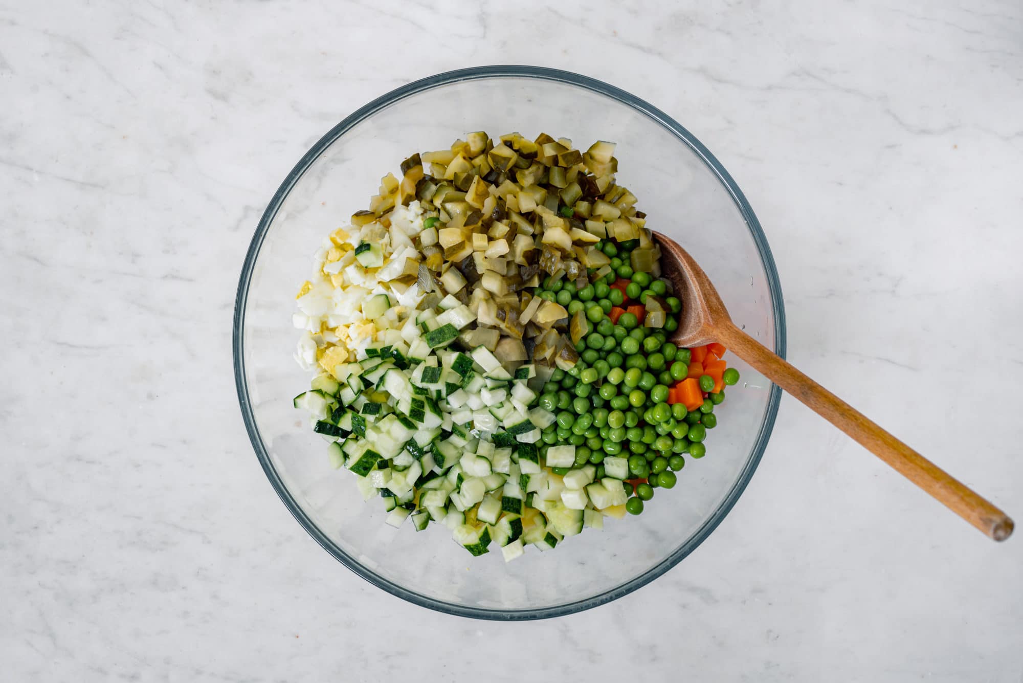 olivier-salad-ingredients-in-a-clear-bowl-with-a-wooden-spoon