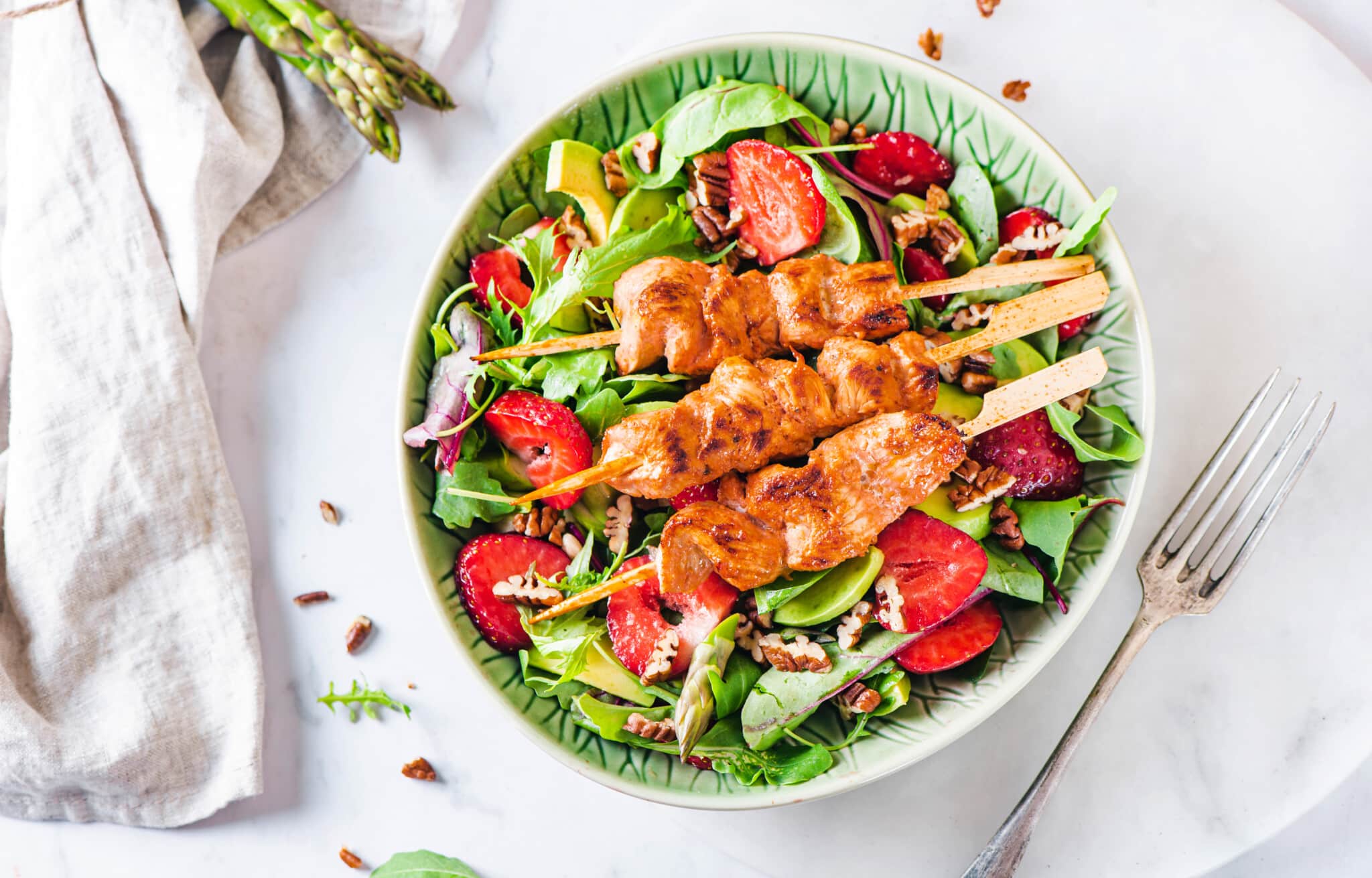 Chicken skewer salad in a bowl with chicken skewers atop a bed of greens.