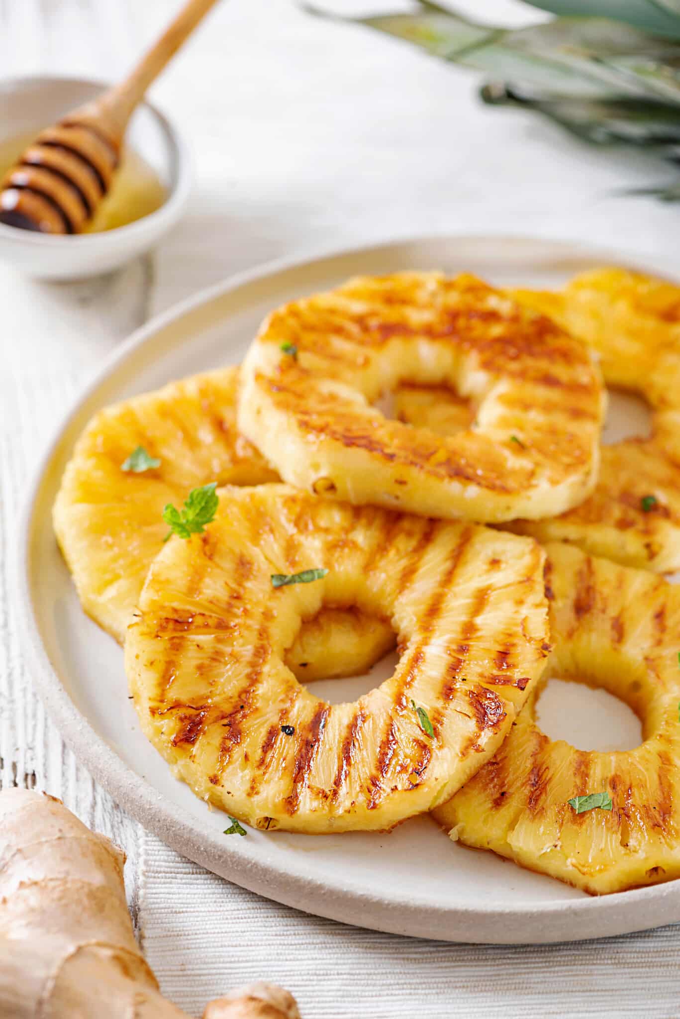 Pineapple slices on a white plate with a bowl of honey.