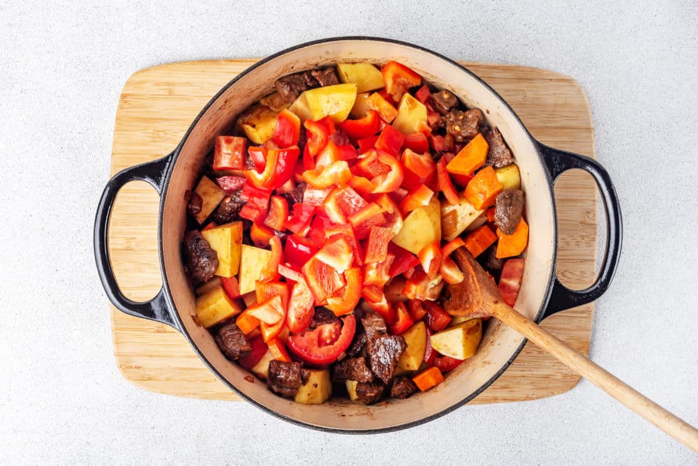 Ingredients all together in a large pot on a wooden board with a wooden spoon in the pot.