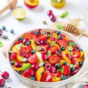 a white bowl filled with chopped summertime salad and mint leaves.