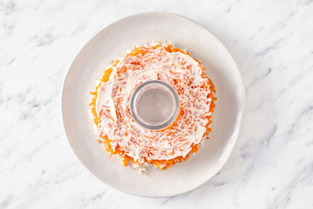 carrots and mayonnaise layer of a salad on a white plate with a glass in the middle to hold the wreath shape.