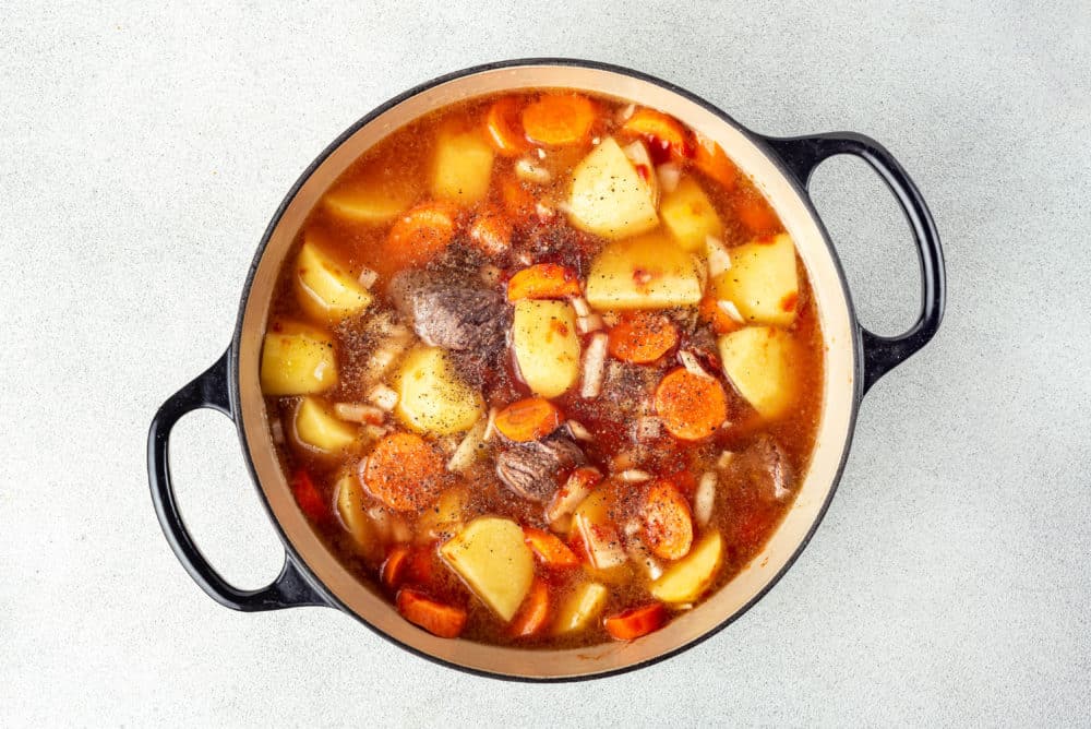 a stew cooking in a pot with spices sprinkled on top.