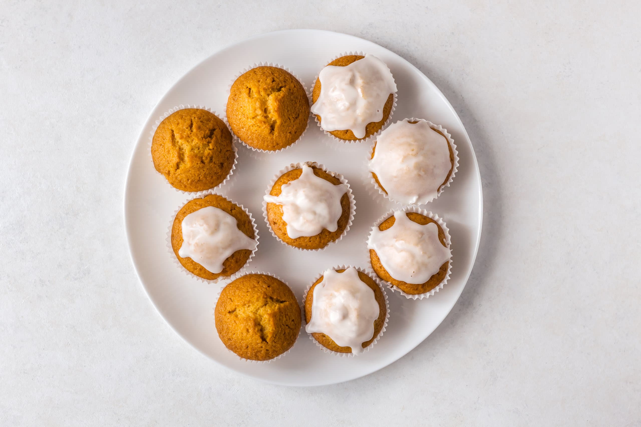 Pumpkin muffins, some glazed, on a white plate.