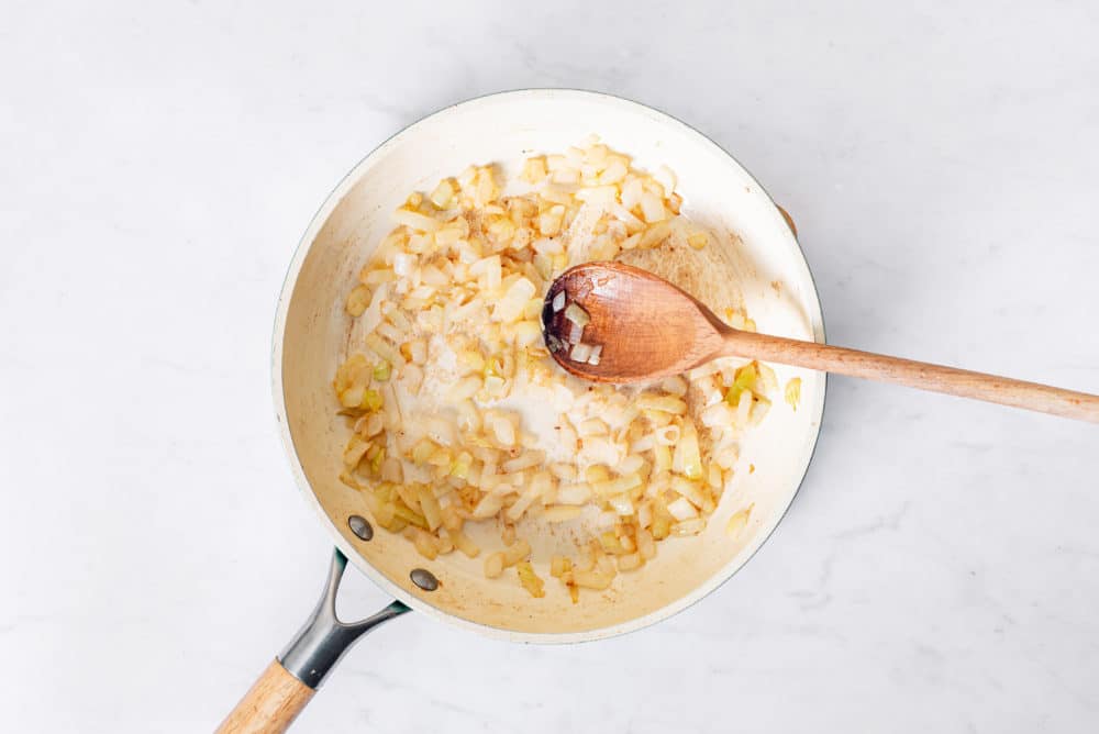 Diced onions sauteing in a skillet with a wooden spoon.