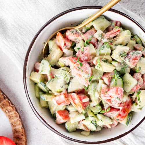 prepared avocado tomato salad in a white bowl with a black rim and a gold spoon on the side.