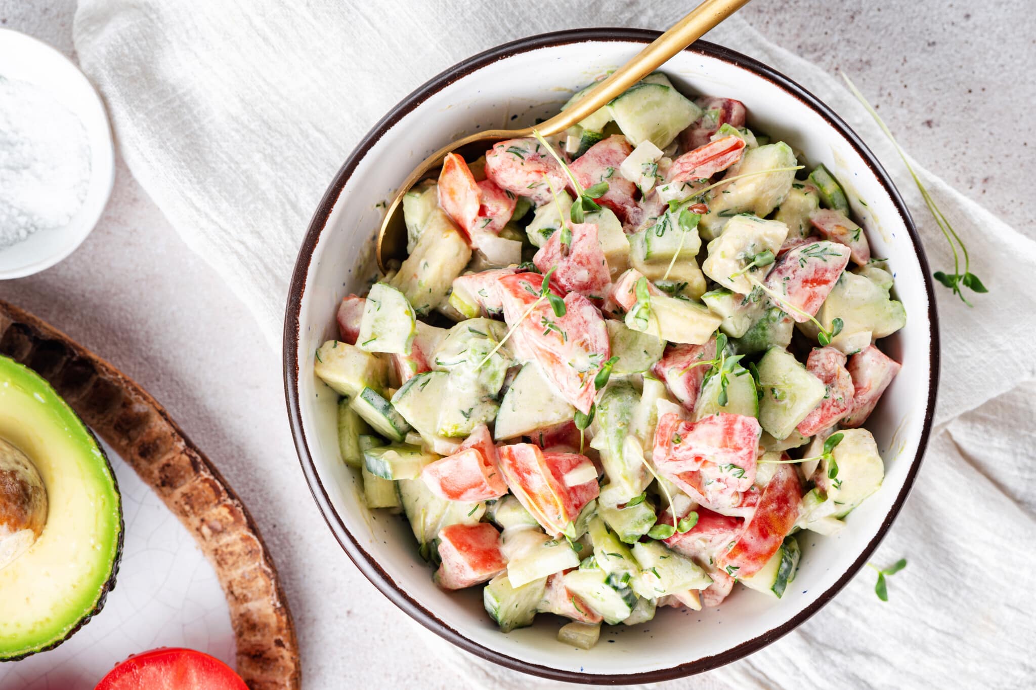 prepared avocado tomato salad in a white bowl with a black rim and a gold spoon on the side.