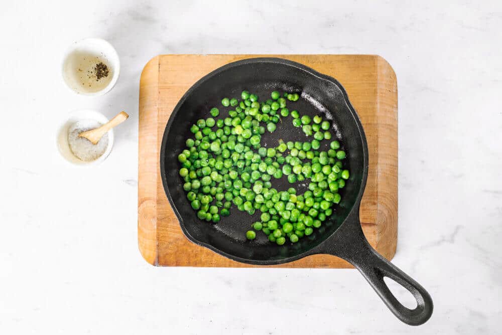 a wooden board with a black skillet on it and peas.