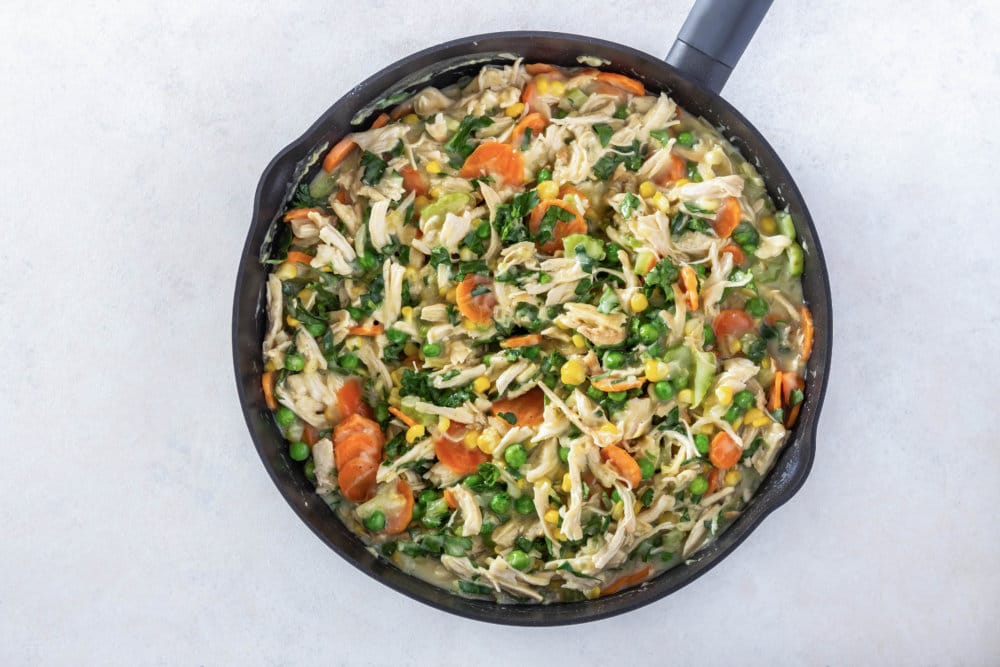 chicken pot pie filling with chicken added in cooking in a skillet.