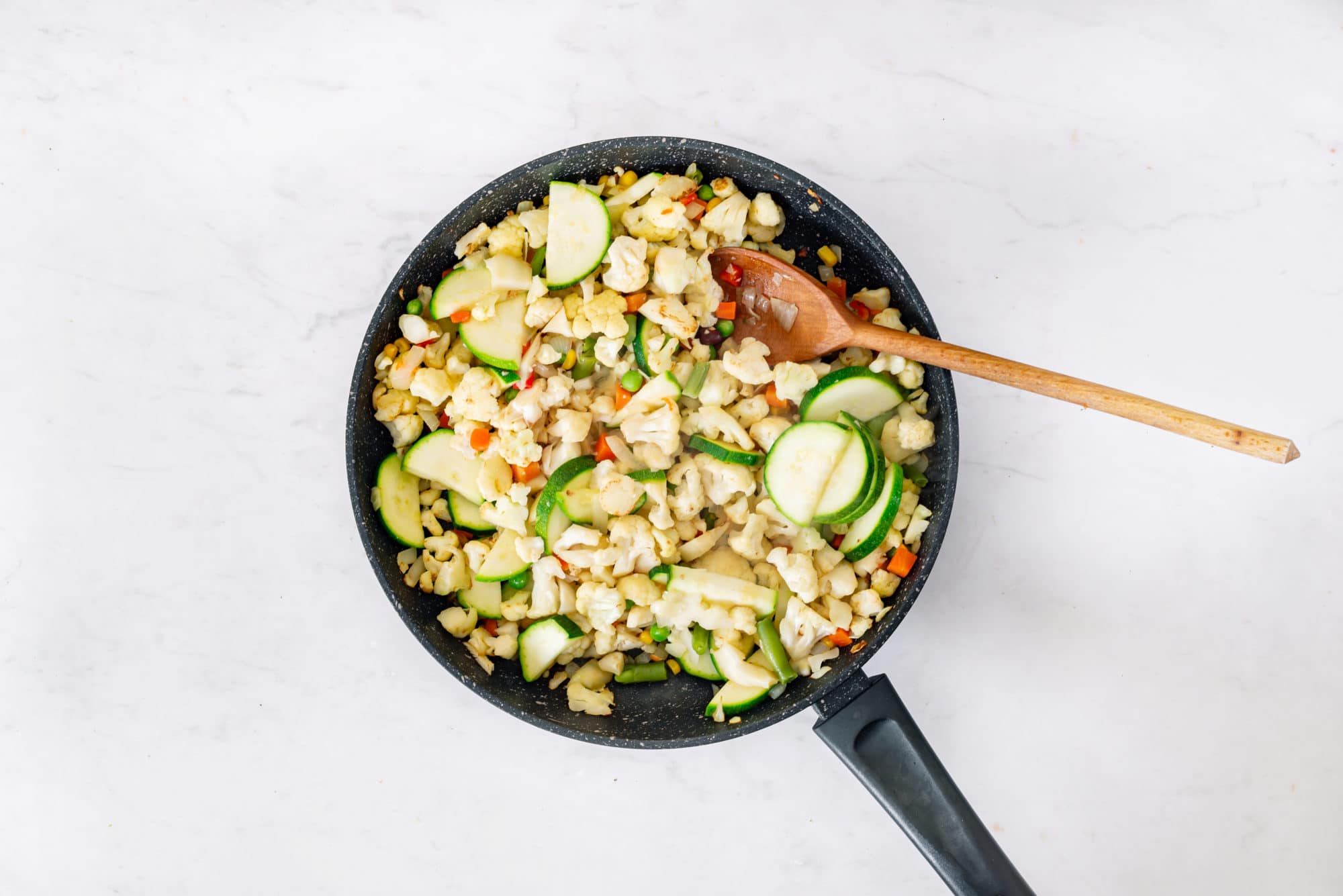 Sauteing cauliflower rice ingredients in a skillet wiht a wooden spoon.