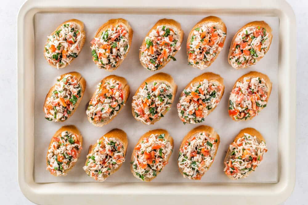 Unbaked bruschetta on a baking sheet lined with parchment paper.