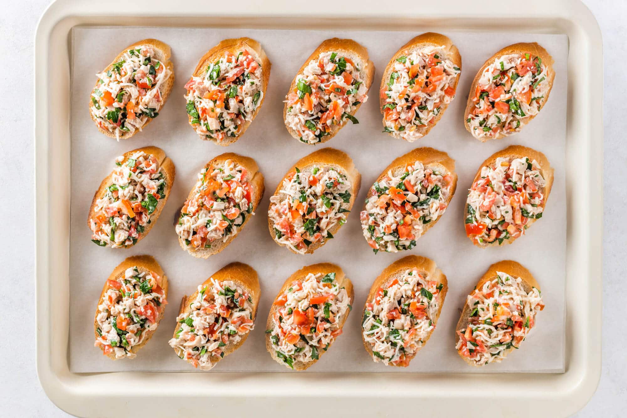 Unbaked bruschetta on baking sheet lined with parchment paper.