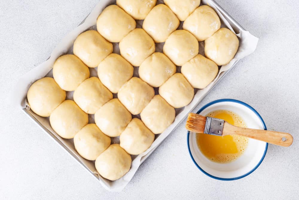 raw-dinner-rolls-on-a-baking-sheet-egg-wash-and-brush-on-the-side