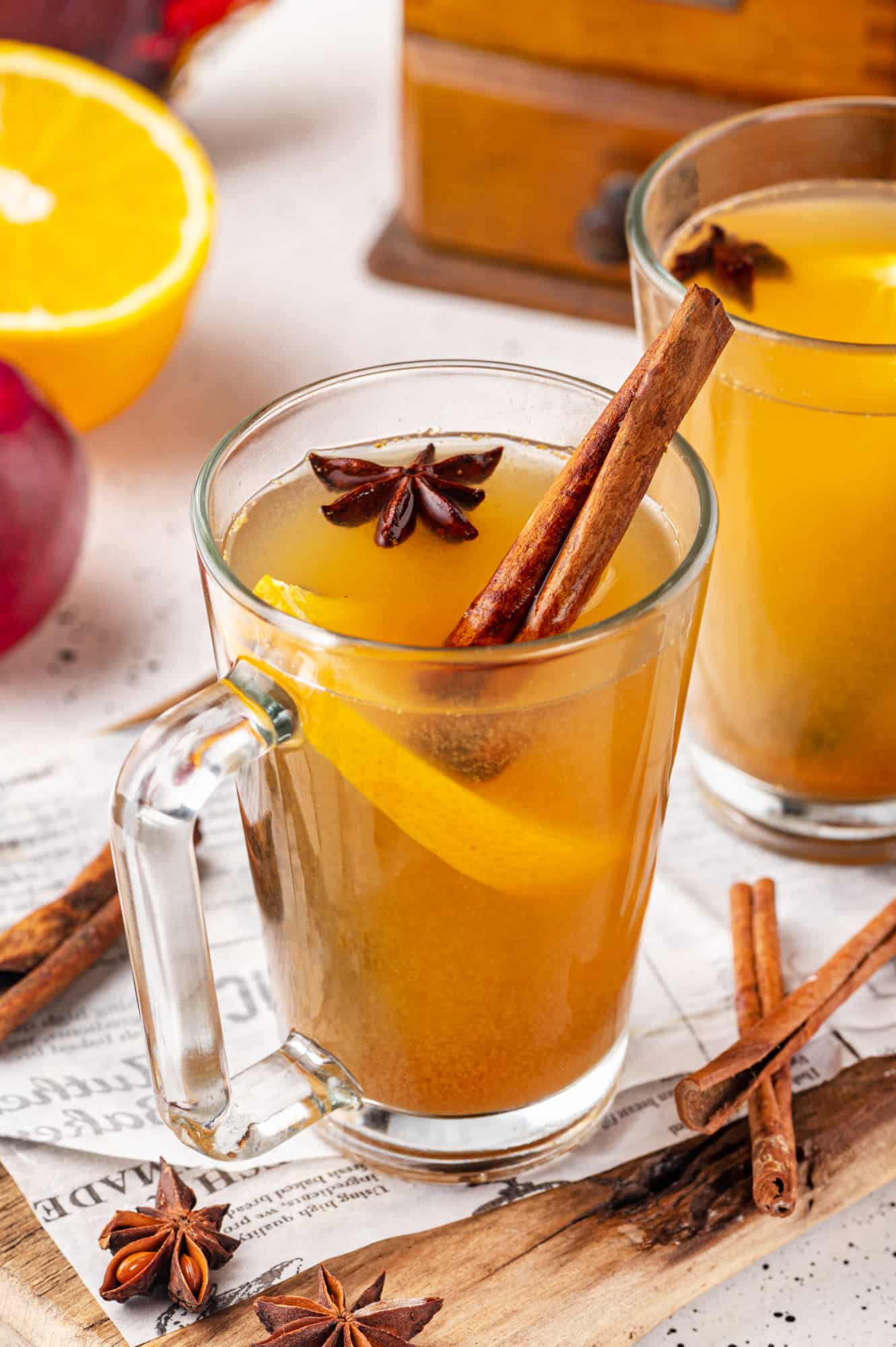 A wooden board with two mugs on it filled with apple cider and with spices floating inside.