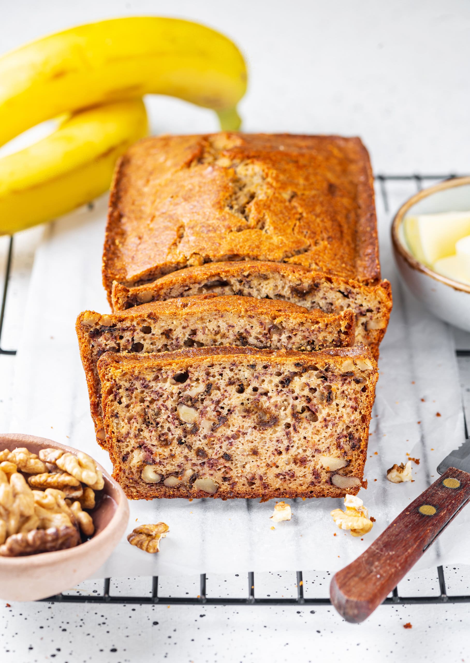 banana bread sliced on a wire rack with a knife.