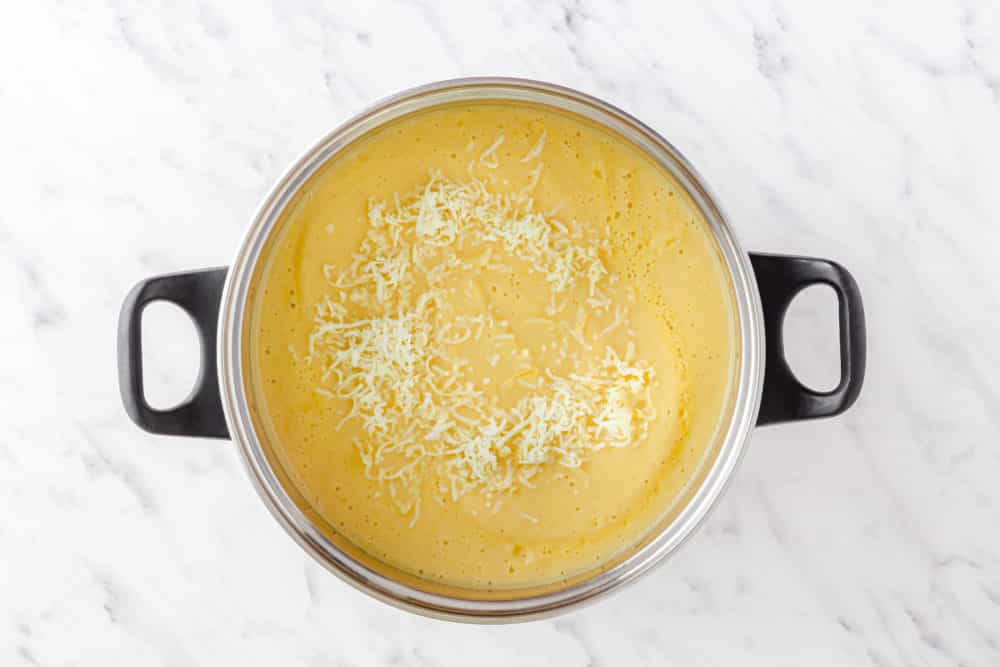 fully blended cauliflower soup in a large soup pot with cheese sprinkled on top.