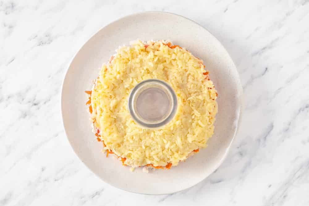 a glass in the center of a white plate creating a shape of a wreath with a potato salad layer atop.