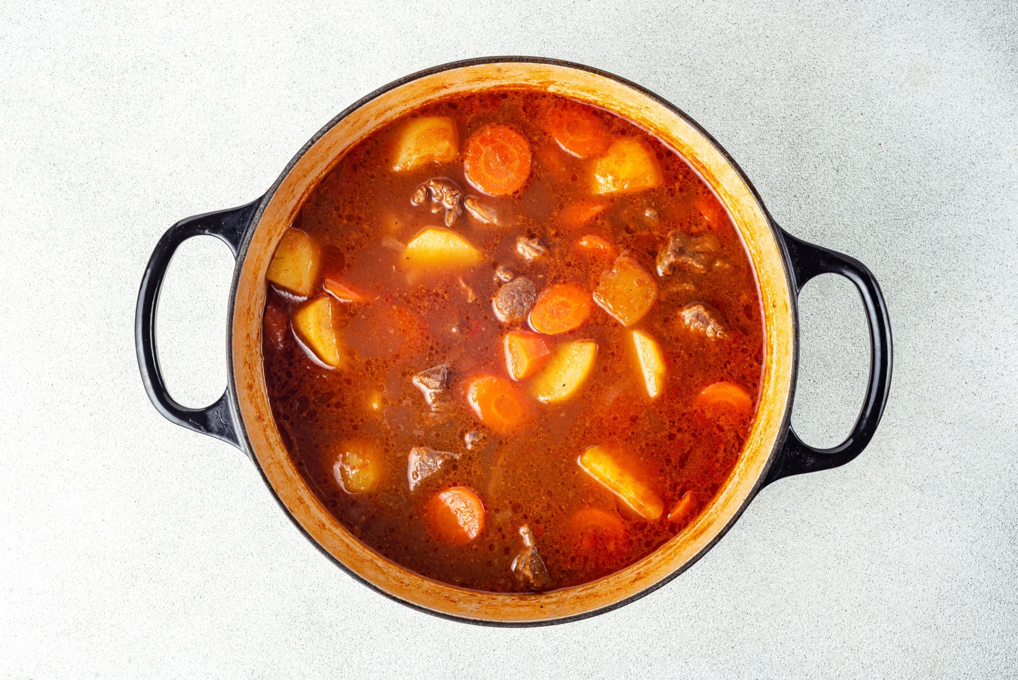 beef stew covered with broth cooking in a large black pot.