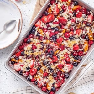 Warm fruit salad in a baking sheet with a spoon on a plate on the side.