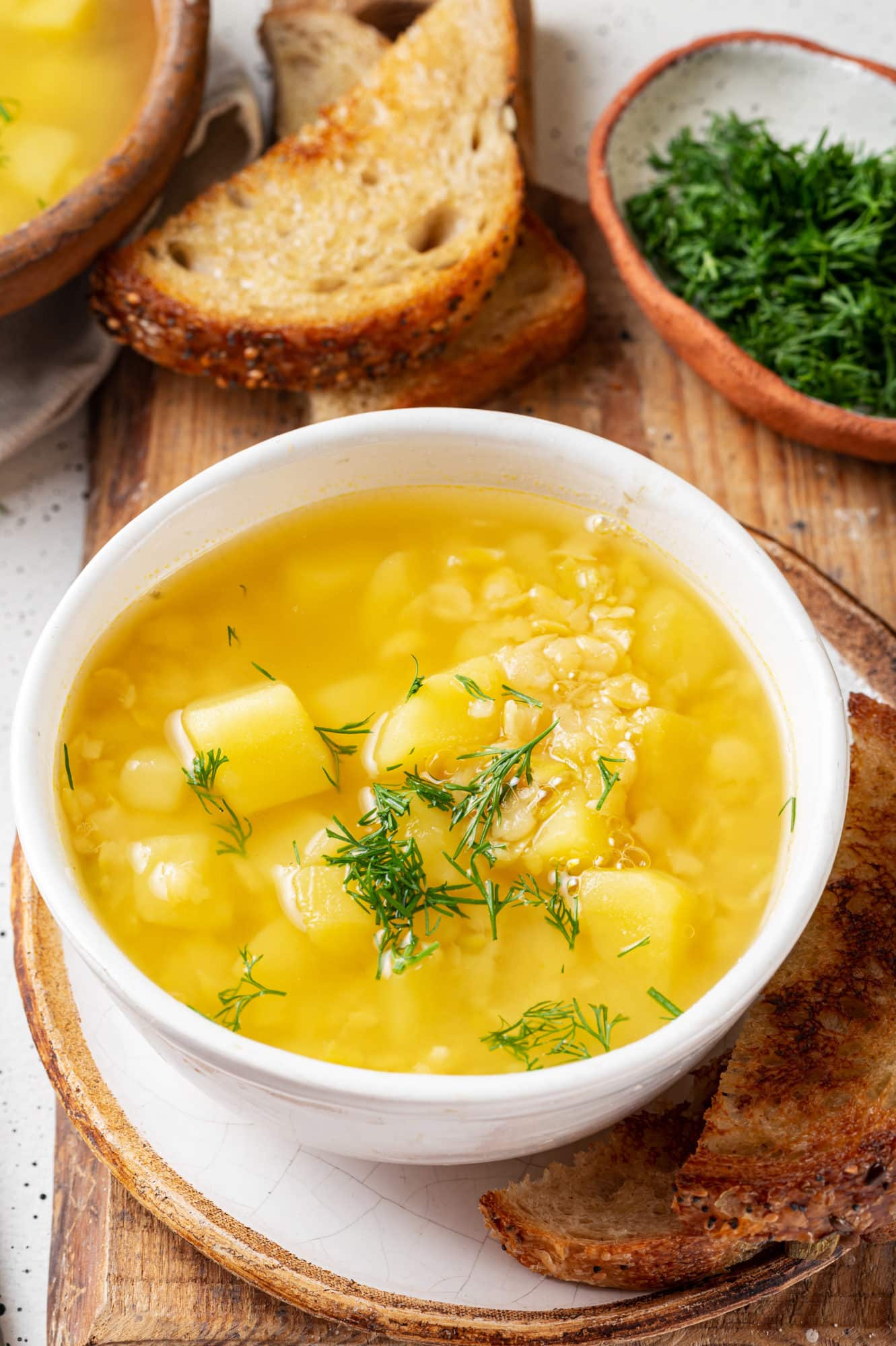 split-pea-soup-in-a-white-bowl-with-toast-slices-all-on-a-wooden-board