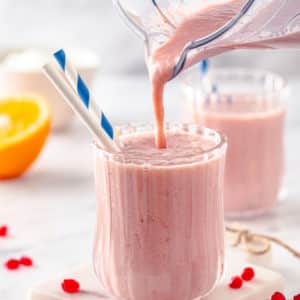 smoothie being poured into a glass cup with straws from a blender.