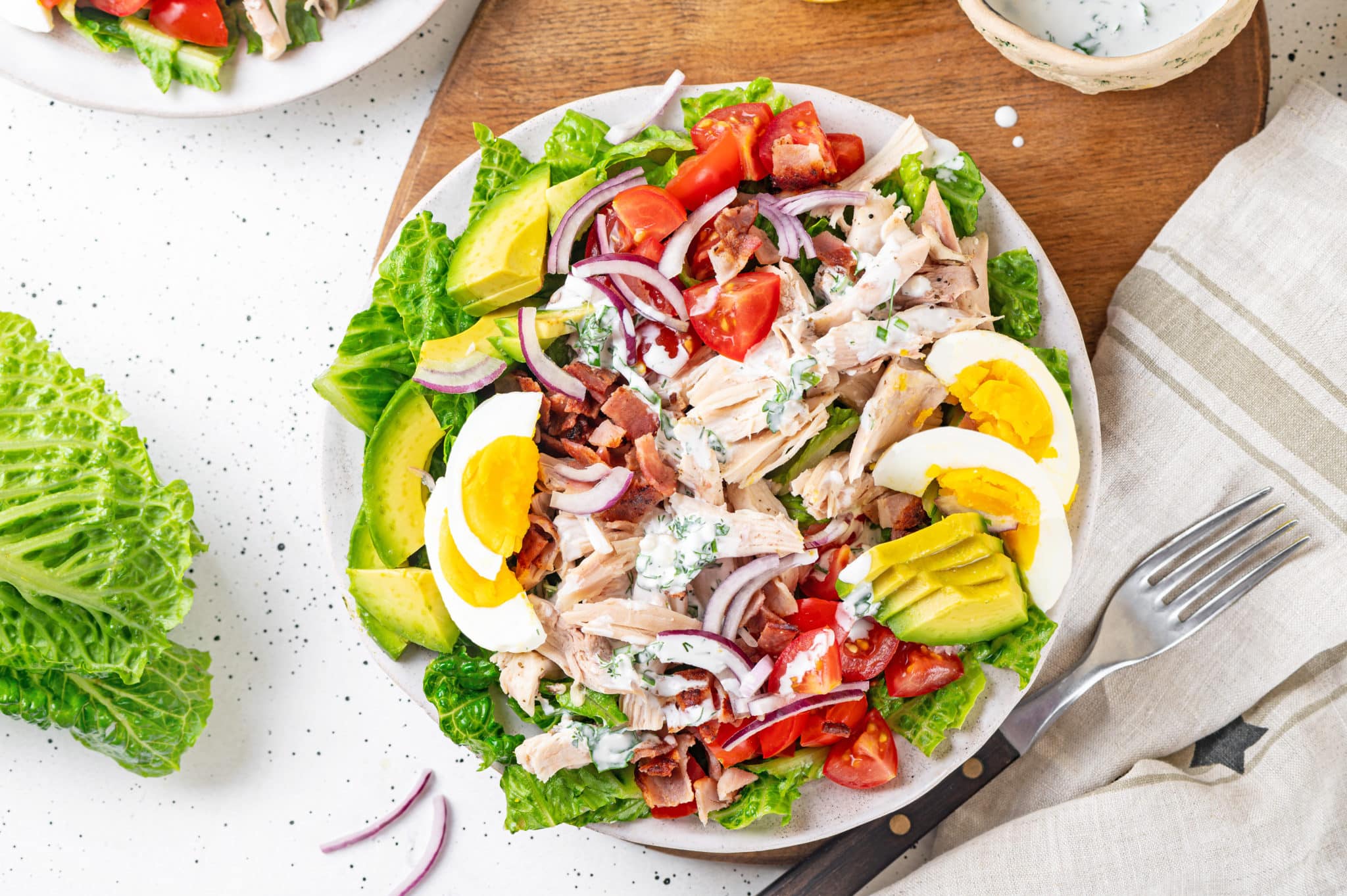 Cobb salad with chicken, tomatoes, and hard boiled eggs on a bed of lettuce on a white plate.