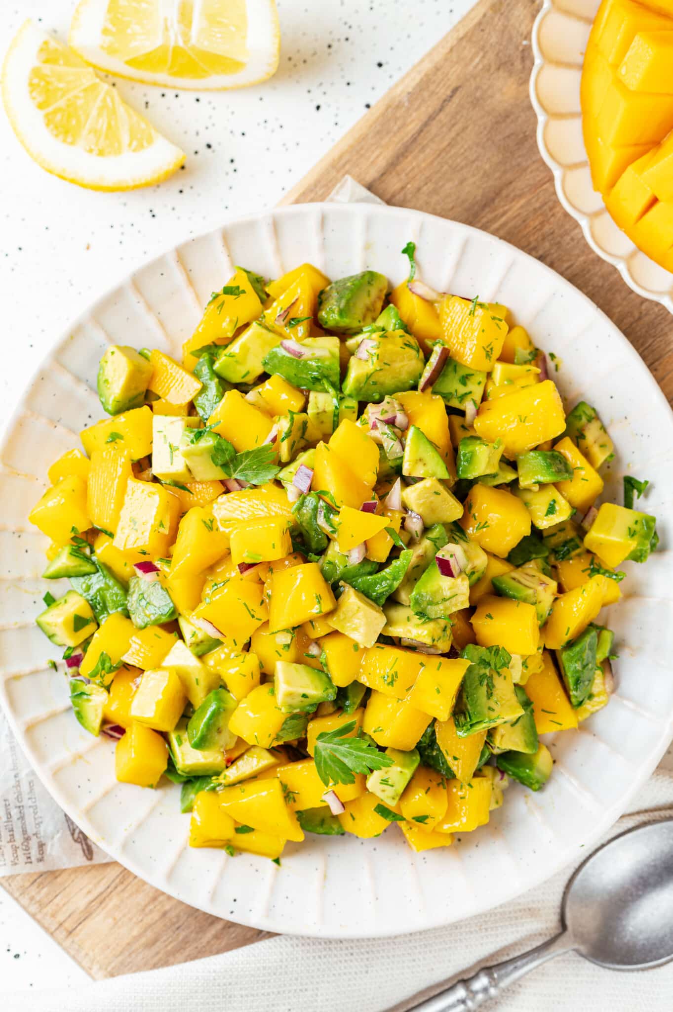 Mango salad with avocado, red onion, dill, and parsley on a white textured plate. 