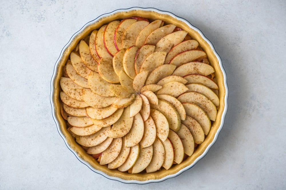 apple slices arranged on top of an apple tart with cinnamon sprinkled on top.