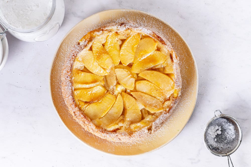 apple sharlotka baked fresh on a beige plate, sprinkled with powdered sugar.