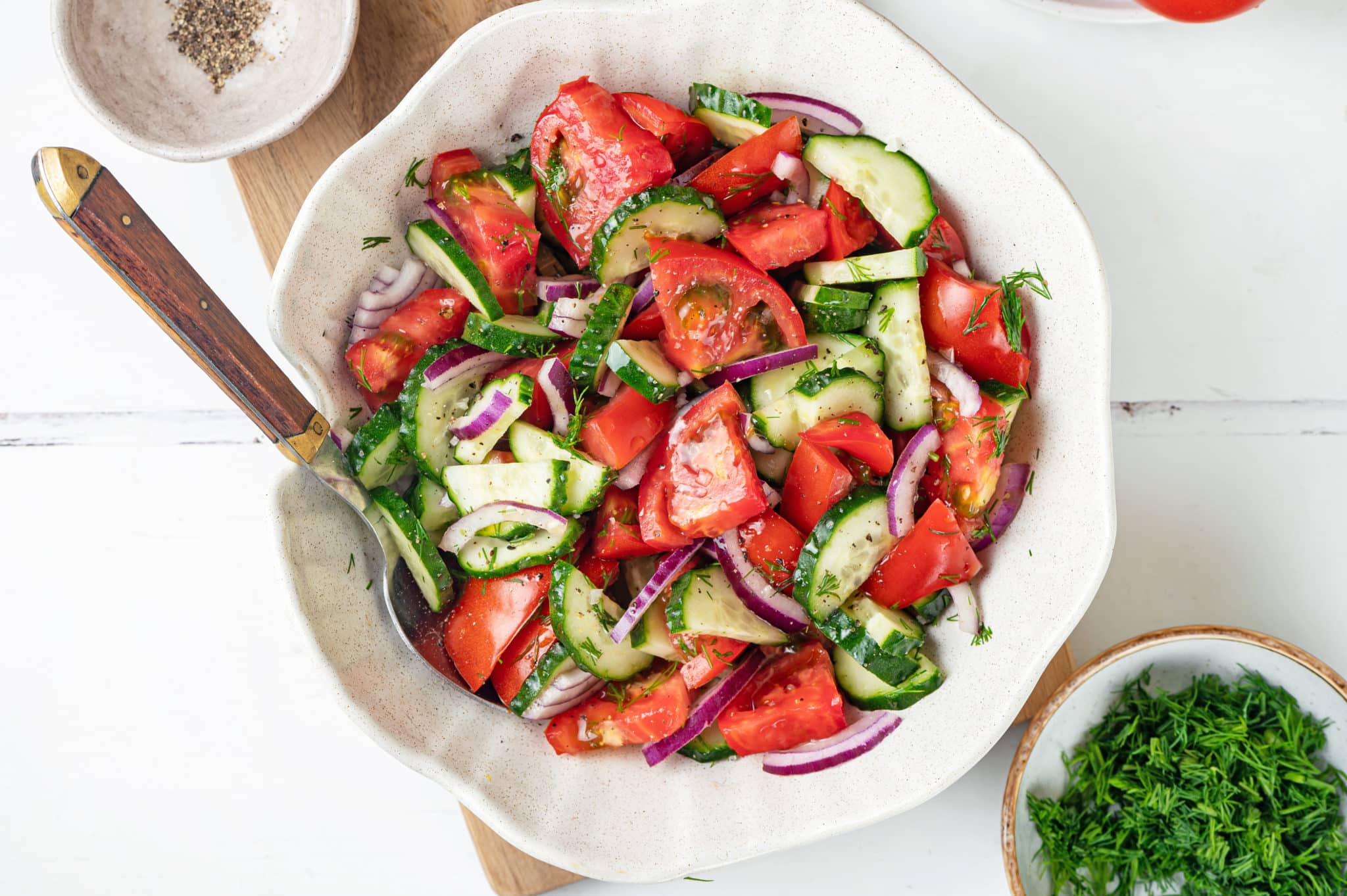 summer-salad-in-a-white-bowl-with-a-spoon-on-a-wooden-board-with-a-bowl-of-dill-on-the-side