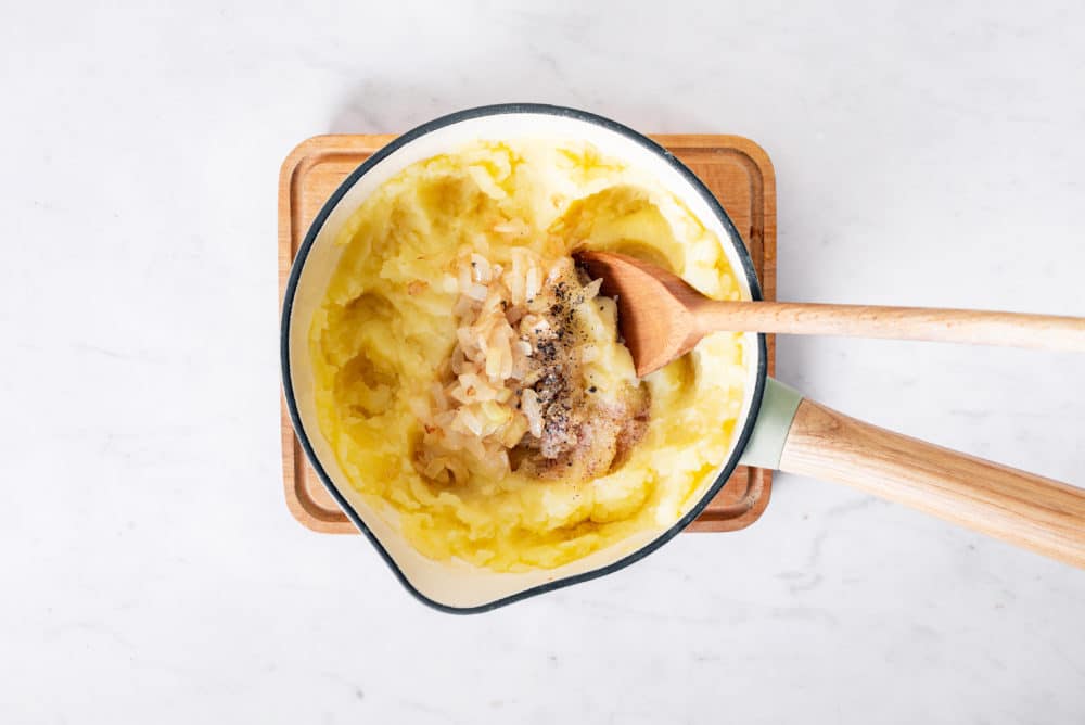 Mashed potato filling with fried onions in a saucepan.