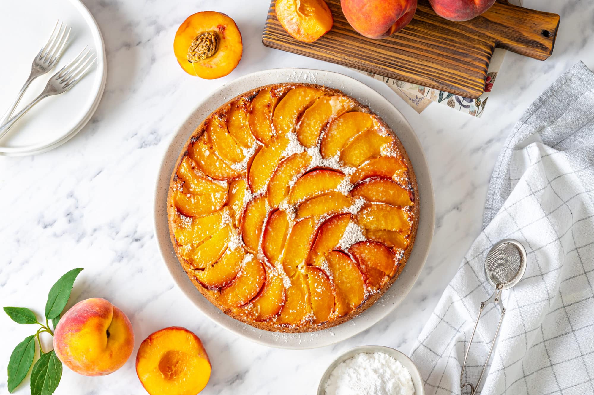 Fluffy peach upside down cake dusted in powdered sugar with peaches on the side.