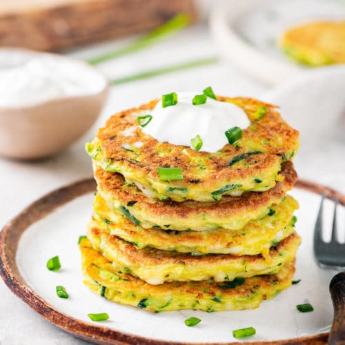 stacked zucchini fritters on a white plate with a fork on the side.