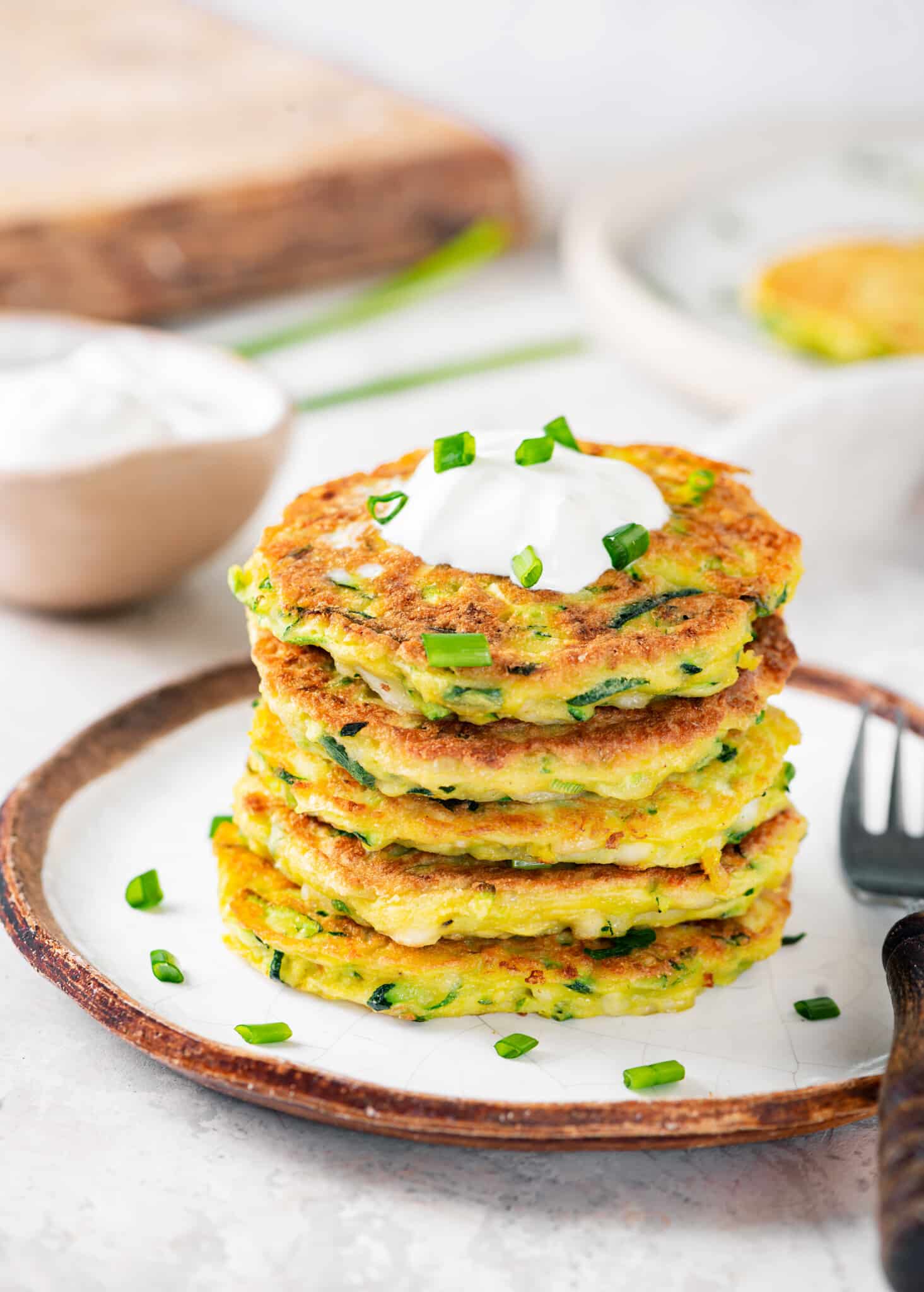 stacked zucchini fritters on a white plate with a fork on the side.