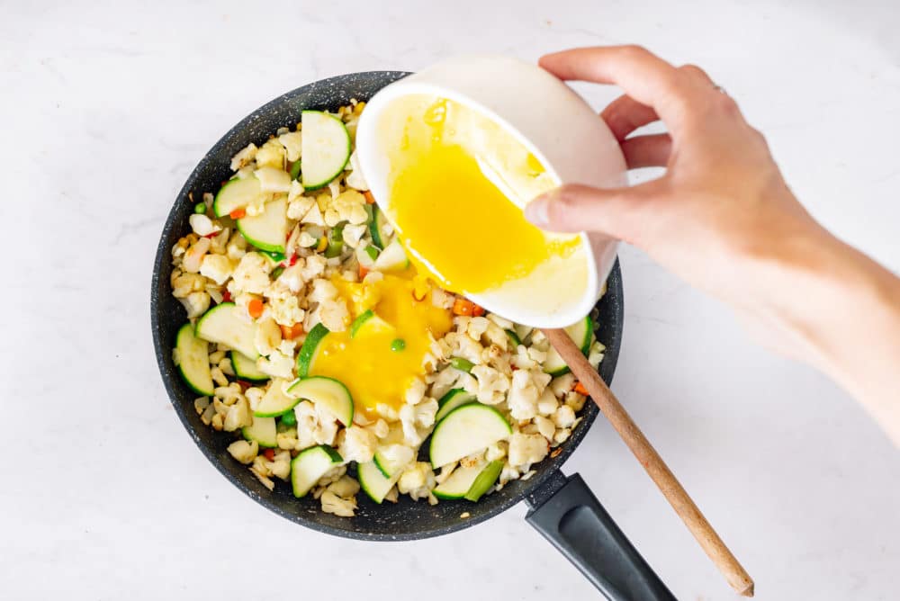 Adding eggs to a skillet of sauteing cauliflower rice.