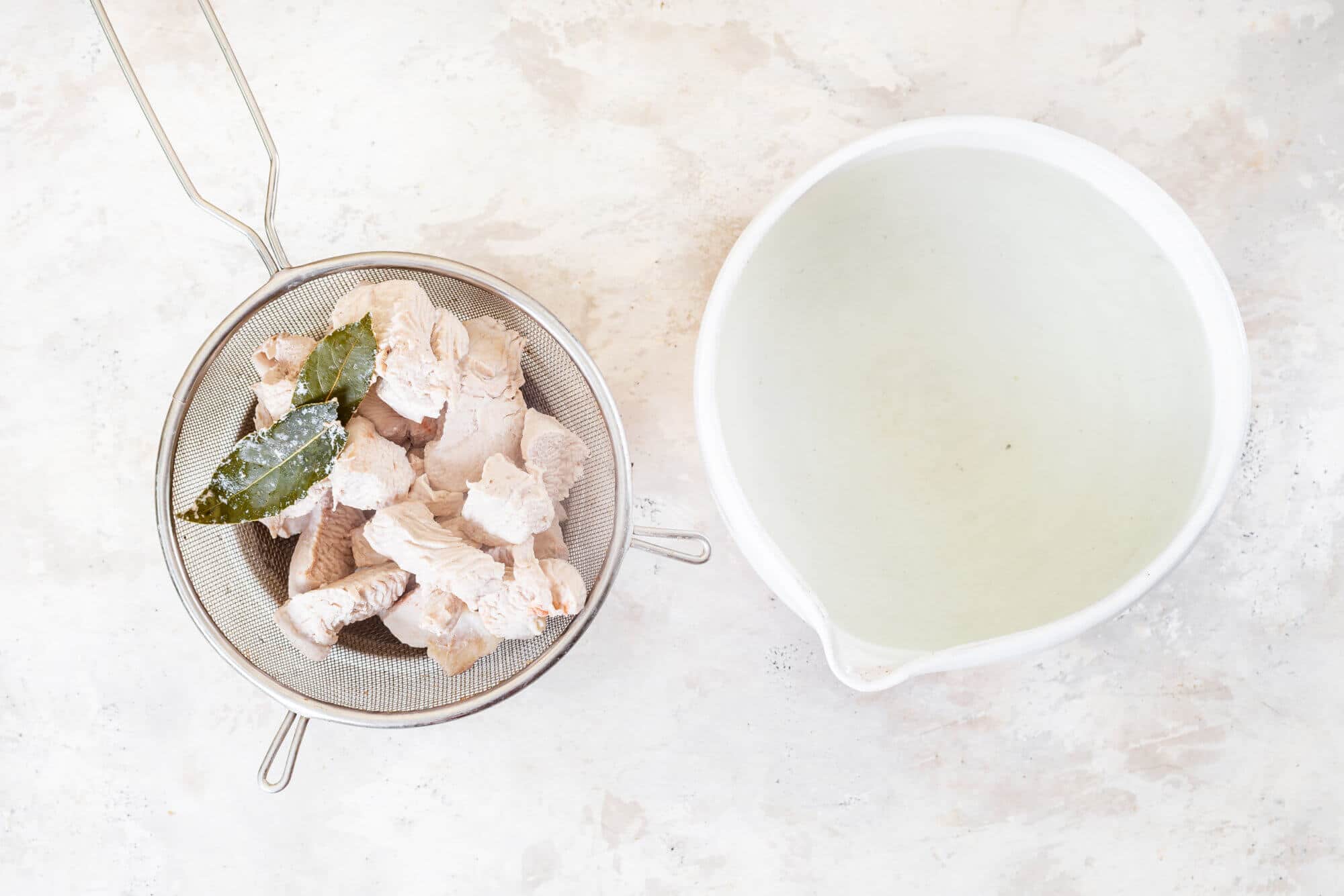 chicken-and-bay-leaves-in-a-sieve-and-water-in-a-white-bowl