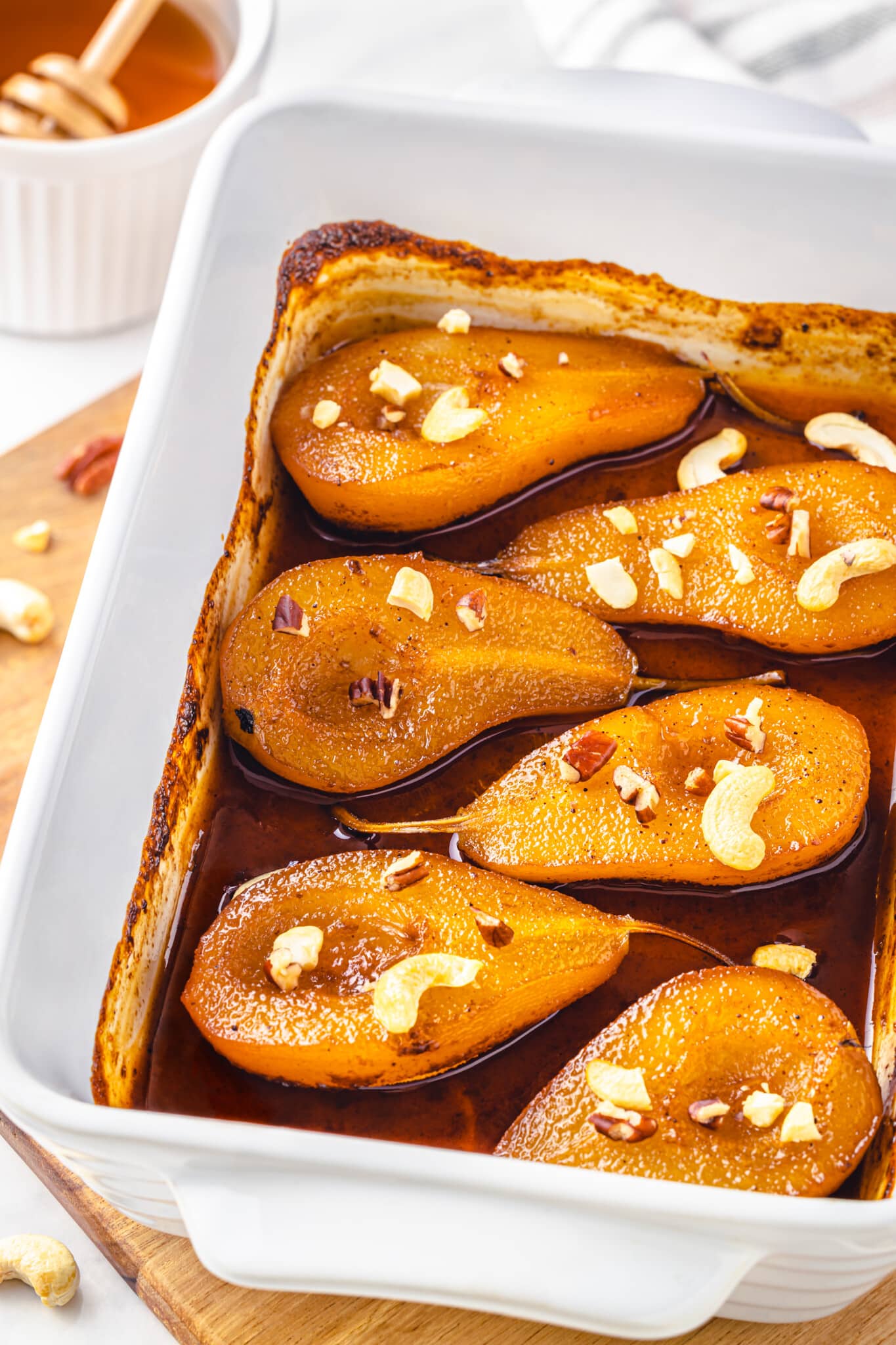 a wooden board with a baking tray on it filled with baked pears honey spice mix and cashews.