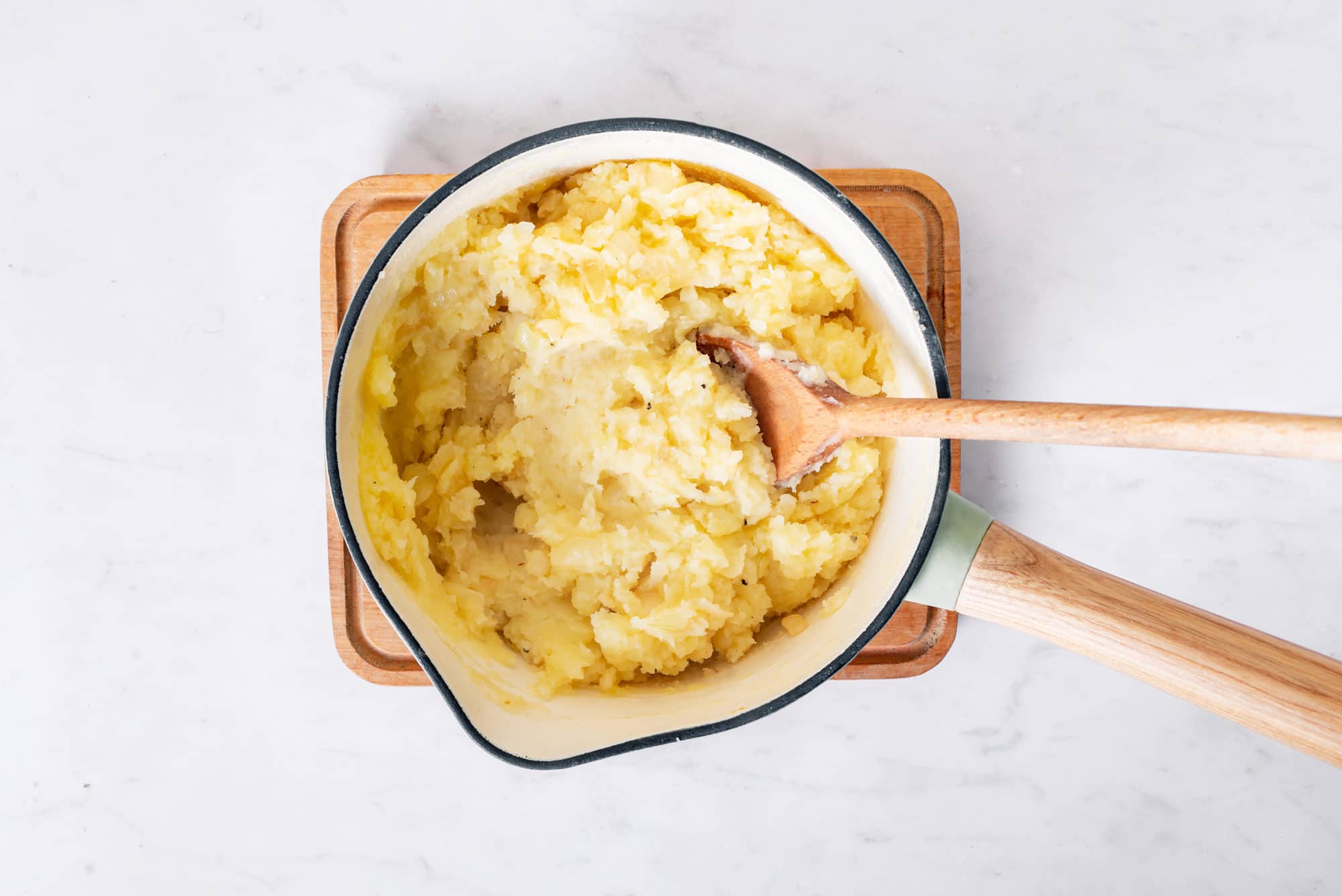 Mashed potato filling in a sauce pan with a wooden spoon.