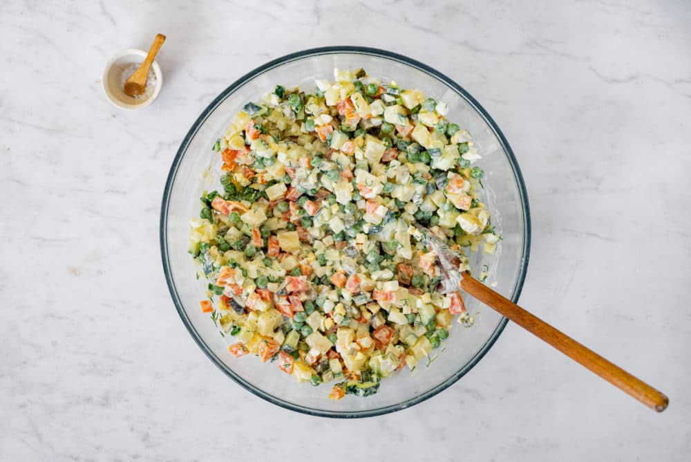 Olivier salad in a glass bowl with a wooden spoon.