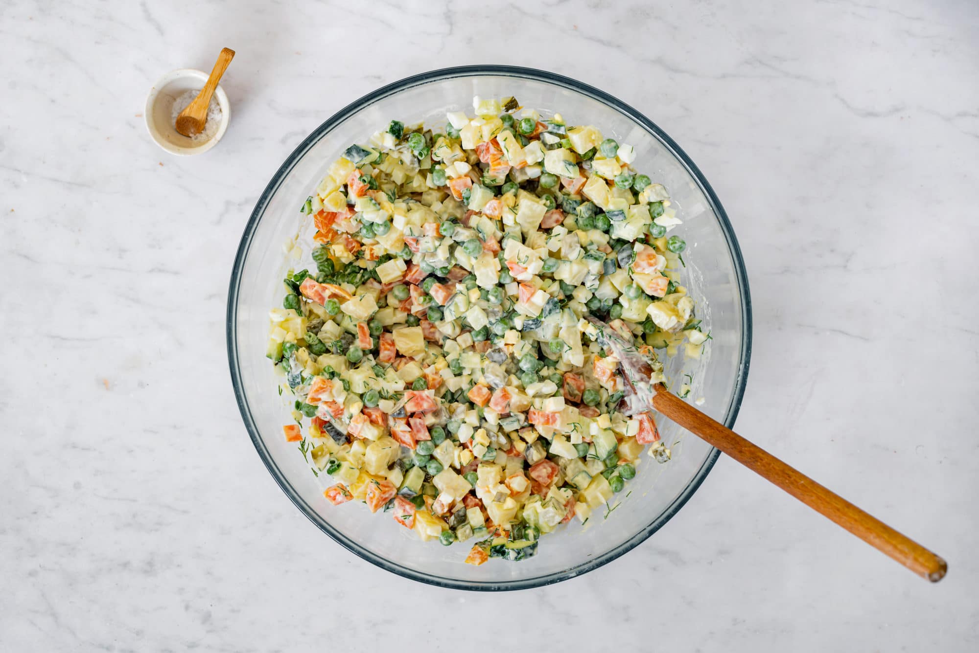 olivier-salad-in-a-clear-bowl-with-a-wooden-spoon-with-a-small-bowl-of-salt-on-the-side