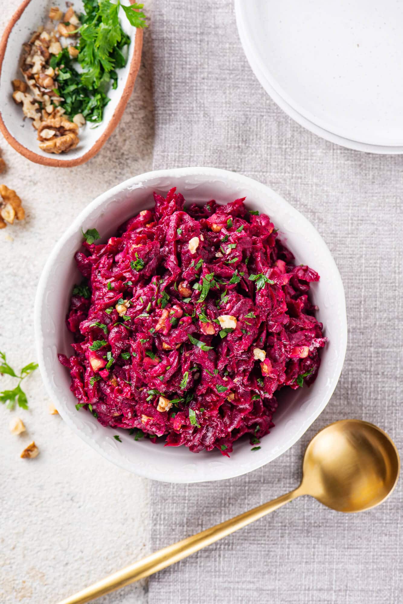 Beet salad in a white bowl with parsley sprinkled on top and extra walnuts.