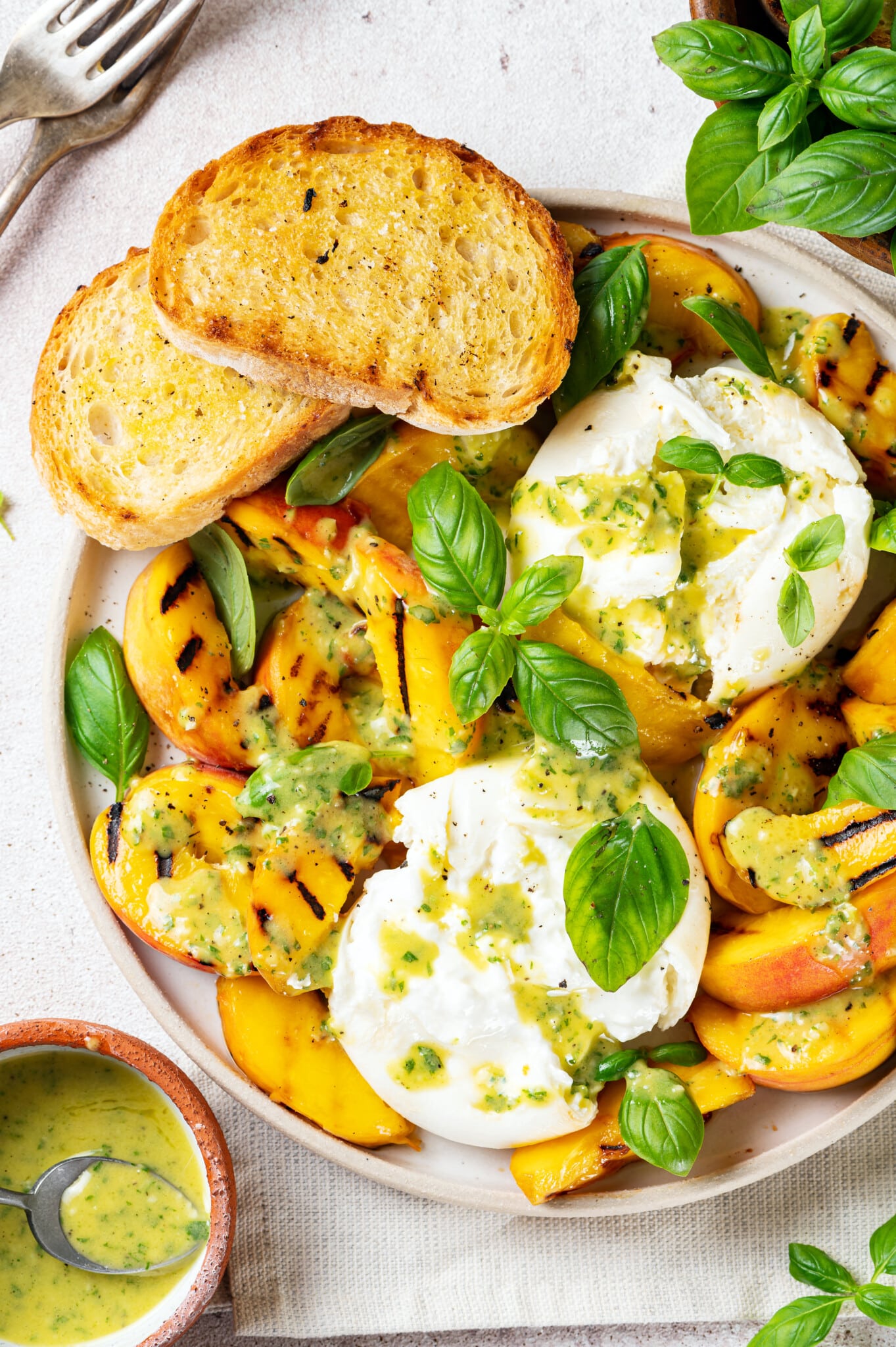 a white plate with grilled peaches burrata cheese balls fresh green basil and salad dressing.